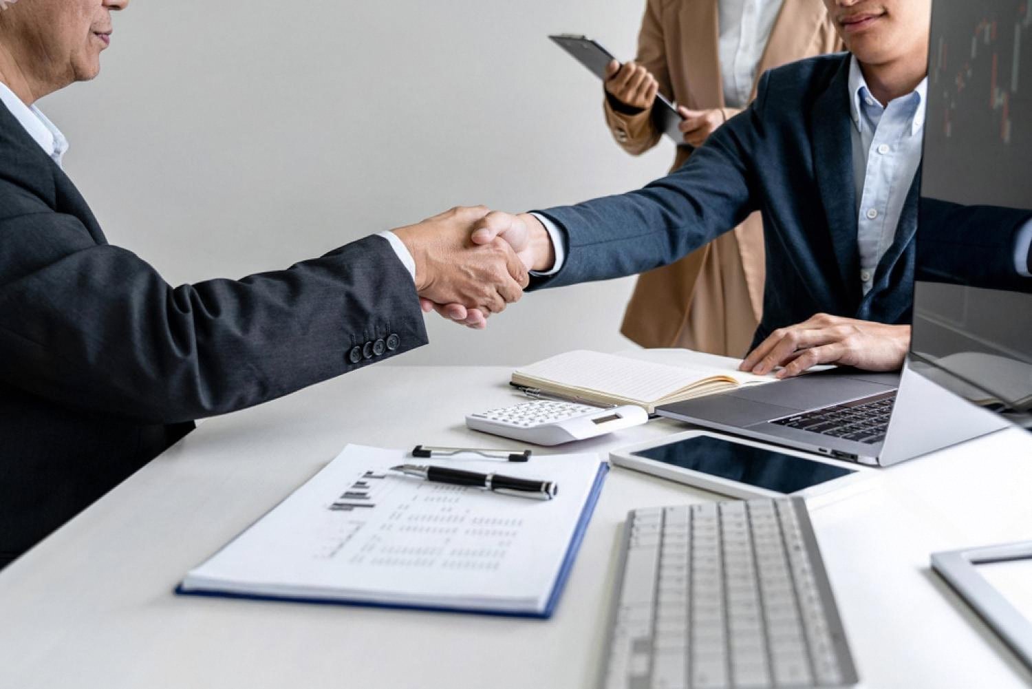 Two executives shaking hands over a UAE risk assessment report with financial charts on the table